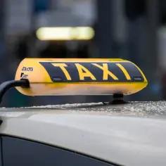 Żółty dachowy znak TAXI na samochodzie, z widocznymi kroplami deszczu.